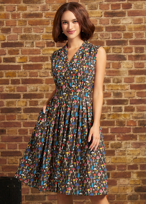 A woman wearing a sleeveless V-neck midi dress with a colorful abstract print, standing in front of a brick wall.