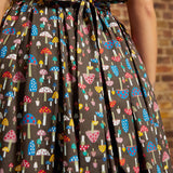Back view of the Carousel Cutie Dress showing the mushroom print, sleeveless bodice, gathered skirt, elastic waist, and adjustable fabric ties knotted at the back waist.