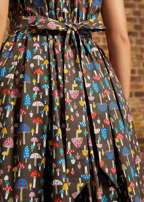 Back view of the Carousel Cutie Dress showing the mushroom print, sleeveless bodice, gathered skirt, elastic waist, and adjustable fabric ties knotted at the back waist.