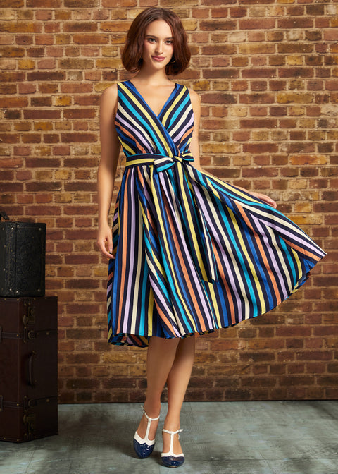 Model wearing ModCloth's Instant Energy Faux-Wrap Dress in Electric Avenue, featuring colorful vertical stripes, a V-neck bodice, tie waist, and flared skirt, paired with blue-and-white heels.