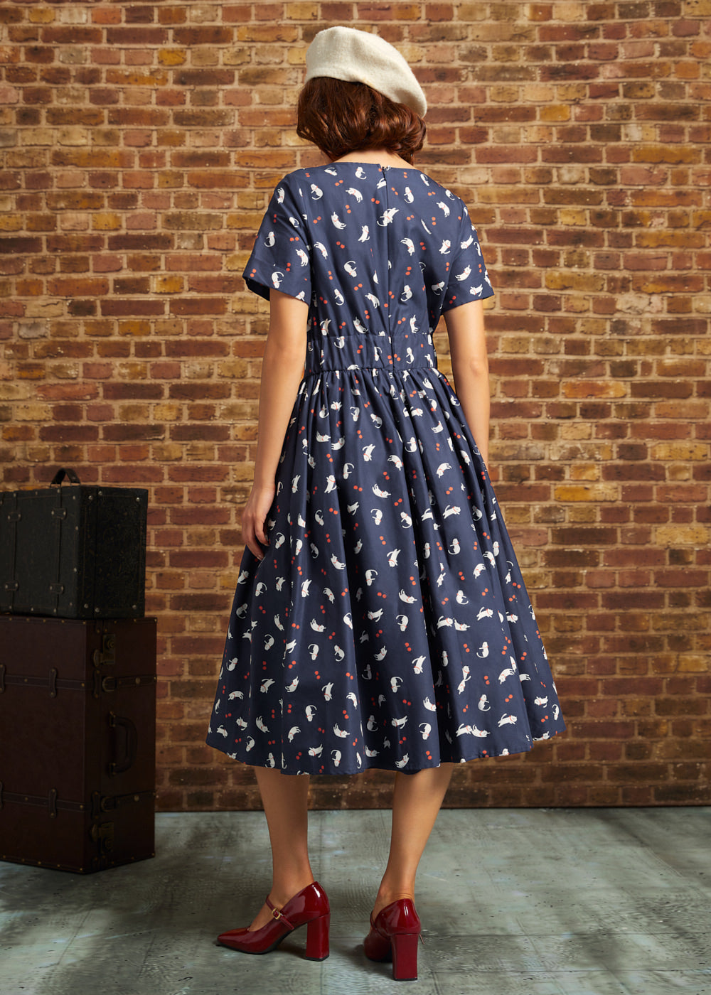 Back view of navy cat and berry print midi dress showing short sleeves, elastic back waist, back zipper, and full gathered skirt.
