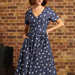 Model wearing a navy cotton fit-and-flare midi dress with white cat and red berry print, V-neckline, short sleeves, and side pockets, styled with a cream beret.