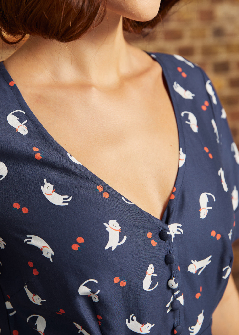 Close-up of the V-neckline and fabric-covered buttons on a navy cotton dress featuring playful white cats and tiny red berries.