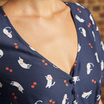 Close-up of the V-neckline and fabric-covered buttons on a navy cotton dress featuring playful white cats and tiny red berries.