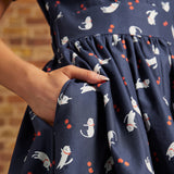 Close-up of a hand tucked into the side pocket of a navy cat print fit-and-flare dress, showing the gathered waist and red berry motifs.