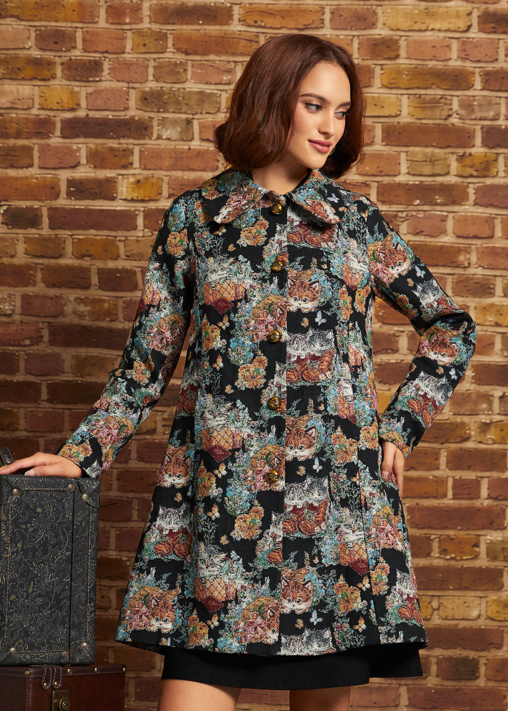 Front view of women's vintage-inspired tapestry coat featuring long sleeves, ornate gold-tone buttons, pointed collar and flared silhouette.