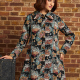Front view of women's vintage-inspired tapestry coat featuring long sleeves, ornate gold-tone buttons, pointed collar and flared silhouette.