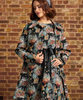 Model wearing ModCloth Timeless Brocade Midi Coat with colorful floral and cat tapestry design, gold buttons and oversized collar, styled with a blue headband