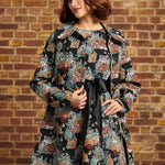 Model wearing ModCloth Timeless Brocade Midi Coat with colorful floral and cat tapestry design, gold buttons and oversized collar, styled with a blue headband