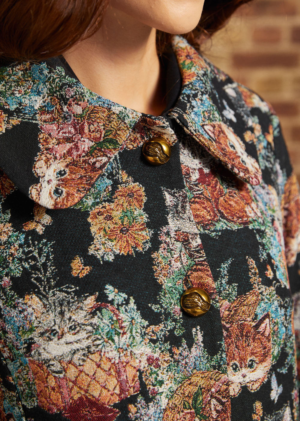 Detail view of oversized pointed collar, decorative gold-tone buttons and intricate cat and floral tapestry design.
