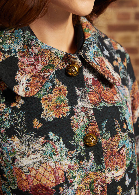 Detail view of oversized pointed collar, decorative gold-tone buttons and intricate cat and floral tapestry design.