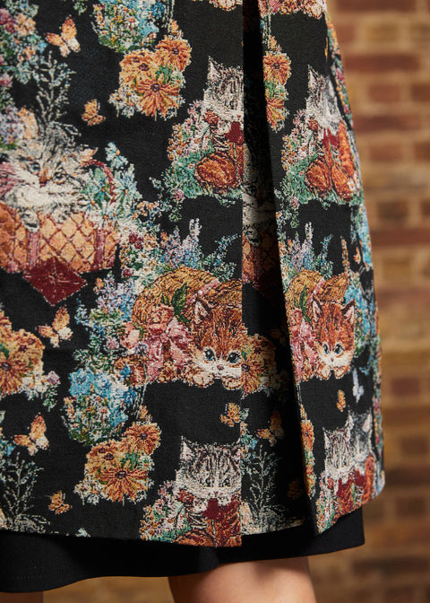 Close-up of tapestry coat hem showing orange and gray kittens among colorful flowers, and back pleat opening.