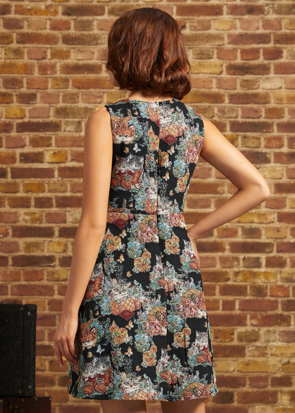 Rear view of the Tallulah mini dress showing its fitted sleeveless bodice, center back zipper, and multicolored cat-and-floral tapestry pattern.