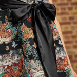 Close-up of the Tallulah mini dress showing its wide black satin sash tied into a bow over the textured kitten tapestry fabric.