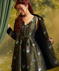 Model wearing the ModCloth Eloise Empire Waist Coat in Catnip Grove, featuring a green woodland cat print, black Peter Pan collar, gold-trimmed buttons, and flared silhouette.