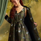 Model wearing an olive-green cat print fit-and-flare dress with its matching printed coat draped over her shoulders, showing the coordinated woodland cat pattern.