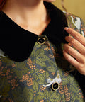 Close-up of the coat's contrasting black Peter Pan collar and gold-rimmed black buttons against the green botanical cat print.