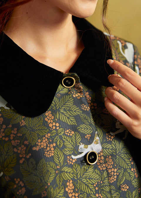 Close-up of the coat's contrasting black Peter Pan collar and gold-rimmed black buttons against the green botanical cat print.