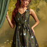 A woman with long red hair models a sleeveless V-neck mini dress with a green and black animal print featuring white cats. She is posed in front of a soft-focus forest background with a green curtain on the left.