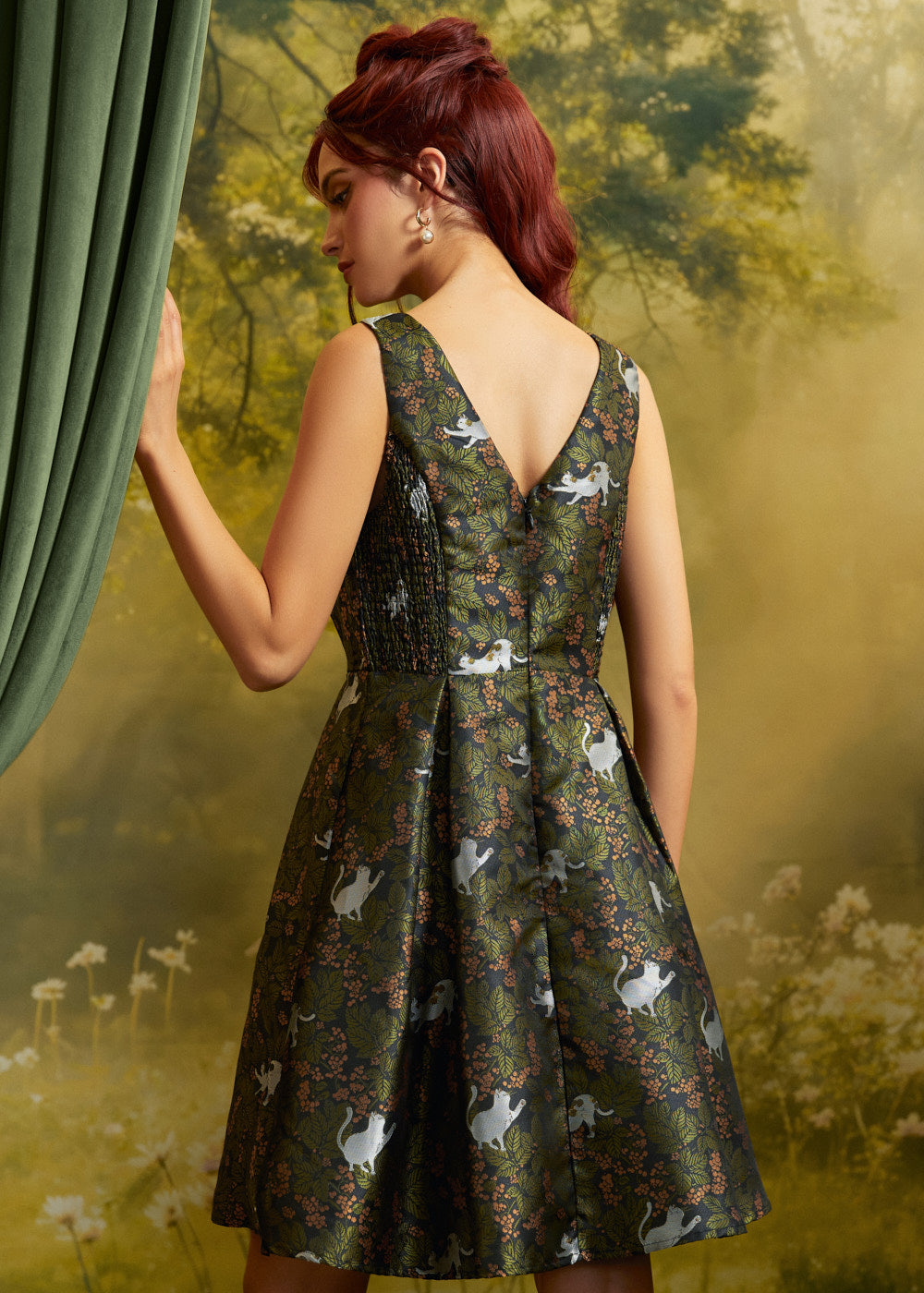Rear three-quarter view of a ModCloth cat print dress showing the V-back, smocked side panel, fitted waist, and flared skirt.
