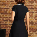 Back view of the Lottie black fit-and-flare dress showing its lace-trimmed collar, short sleeves, fitted waist, and flared skirt.