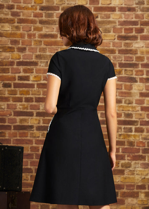 Back view of the Lottie black fit-and-flare dress showing its lace-trimmed collar, short sleeves, fitted waist, and flared skirt.