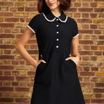 Model standing with hands in the lace-trimmed side pockets of the Lottie black fit-and-flare dress, highlighting its flower-button bodice and flared skirt.