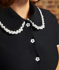 Close-up of the Lottie Dress showing its black Peter Pan collar with scalloped white lace trim and white flower-shaped buttons along the bodice.