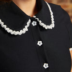 Close-up of the Lottie Dress showing its black Peter Pan collar with scalloped white lace trim and white flower-shaped buttons along the bodice.