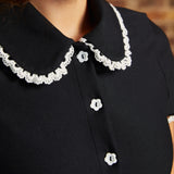 Close-up of the Lottie Dress showing its black Peter Pan collar with scalloped white lace trim and white flower-shaped buttons along the bodice.