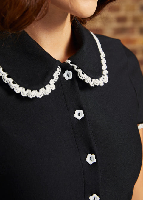 Close-up of the Lottie Dress showing its black Peter Pan collar with scalloped white lace trim and white flower-shaped buttons along the bodice.