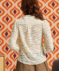 Back view of woman wearing cream floral lace blouse, showing the sheer floral pattern, gathered shoulders, and long puff sleeves.