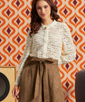 Woman wearing cream floral lace puff sleeve blouse tucked into a brown midi skirt with tie waist and pockets.