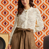 Woman wearing cream floral lace puff sleeve blouse tucked into a brown midi skirt with tie waist and pockets.