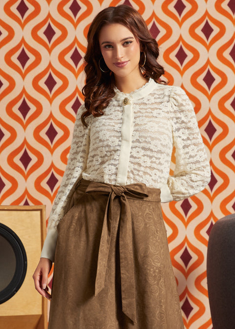 Woman wearing cream floral lace puff sleeve blouse tucked into a brown midi skirt with tie waist and pockets.