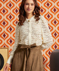 Woman wearing a cream floral lace blouse with high neckline, cameo-style accent, puff sleeves, and long button cuffs.