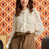 Woman wearing a cream floral lace blouse with high neckline, cameo-style accent, puff sleeves, and long button cuffs.