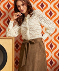 A woman models a white lace long-sleeve blouse and a brown patterned skirt against a retro orange and burgundy patterned wallpaper background.