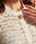 Close-up of cream floral lace blouse showing the lace-trimmed neckline, cameo-style accent, and contrast front placket.