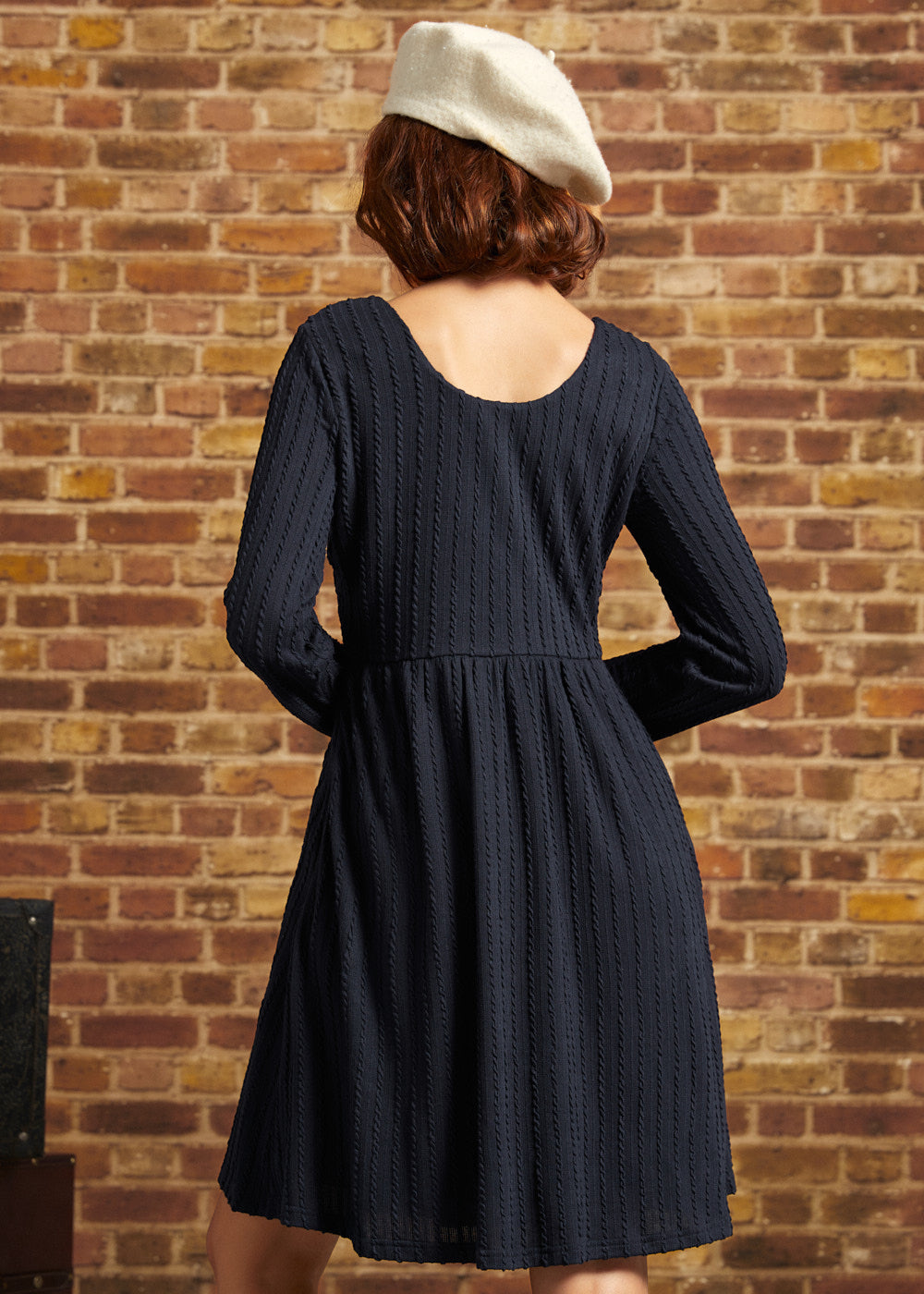 Back view of navy long sleeve knit dress showing scoop back neckline, empire waist seam and flared skirt.