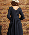 Back view of navy long sleeve knit dress showing scoop back neckline, empire waist seam and flared skirt.