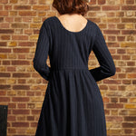 Back view of navy long sleeve knit dress showing scoop back neckline, empire waist seam and flared skirt.