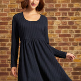 Model wearing a navy cable-textured long sleeve fit-and-flare mini dress with a scoop neckline and empire waist, styled with a white beret.