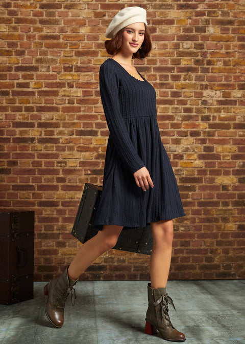 Three-quarter side view of model wearing navy cable-knit fit-and-flare dress with ankle boots and white beret.