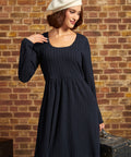 A woman wearing a dark navy blue cable-knit dress and a cream-colored beret, posing in front of a rustic brick wall.
