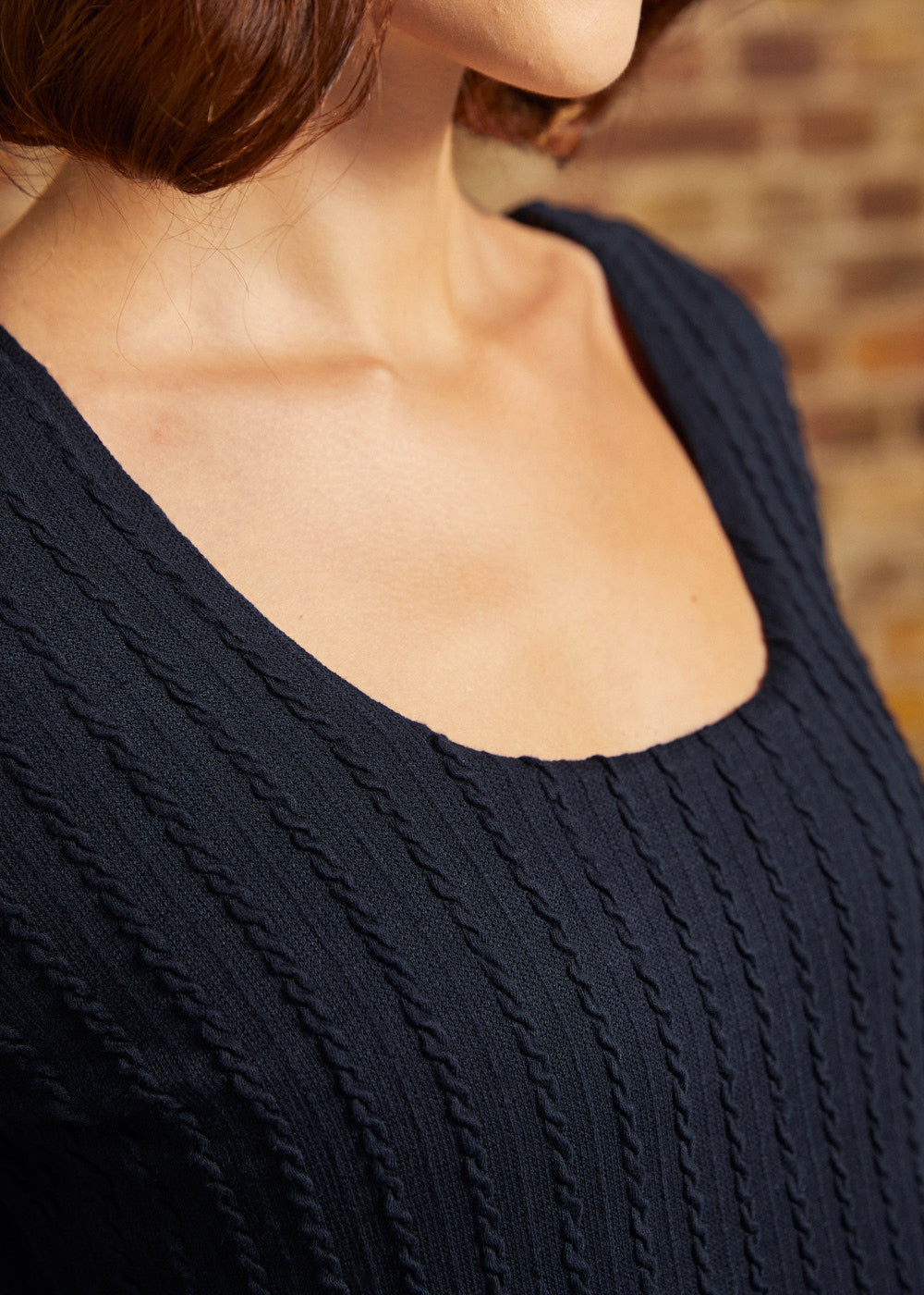 Close-up of scoop neckline and raised vertical cable-knit texture on navy dress.