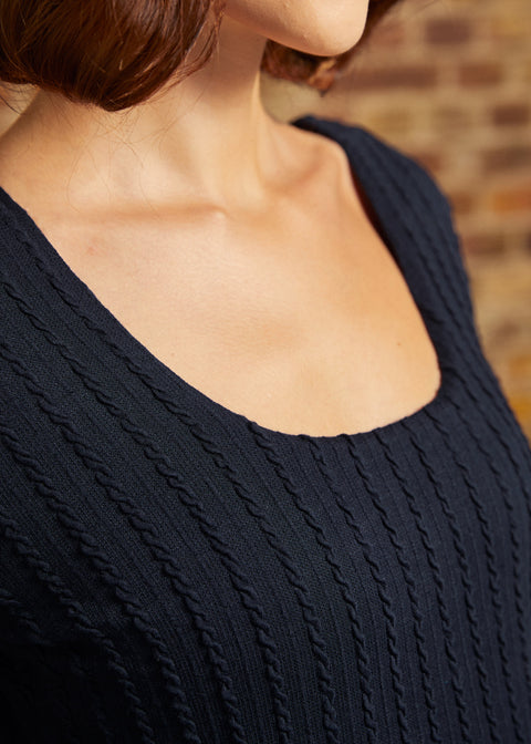 Close-up of scoop neckline and raised vertical cable-knit texture on navy dress.