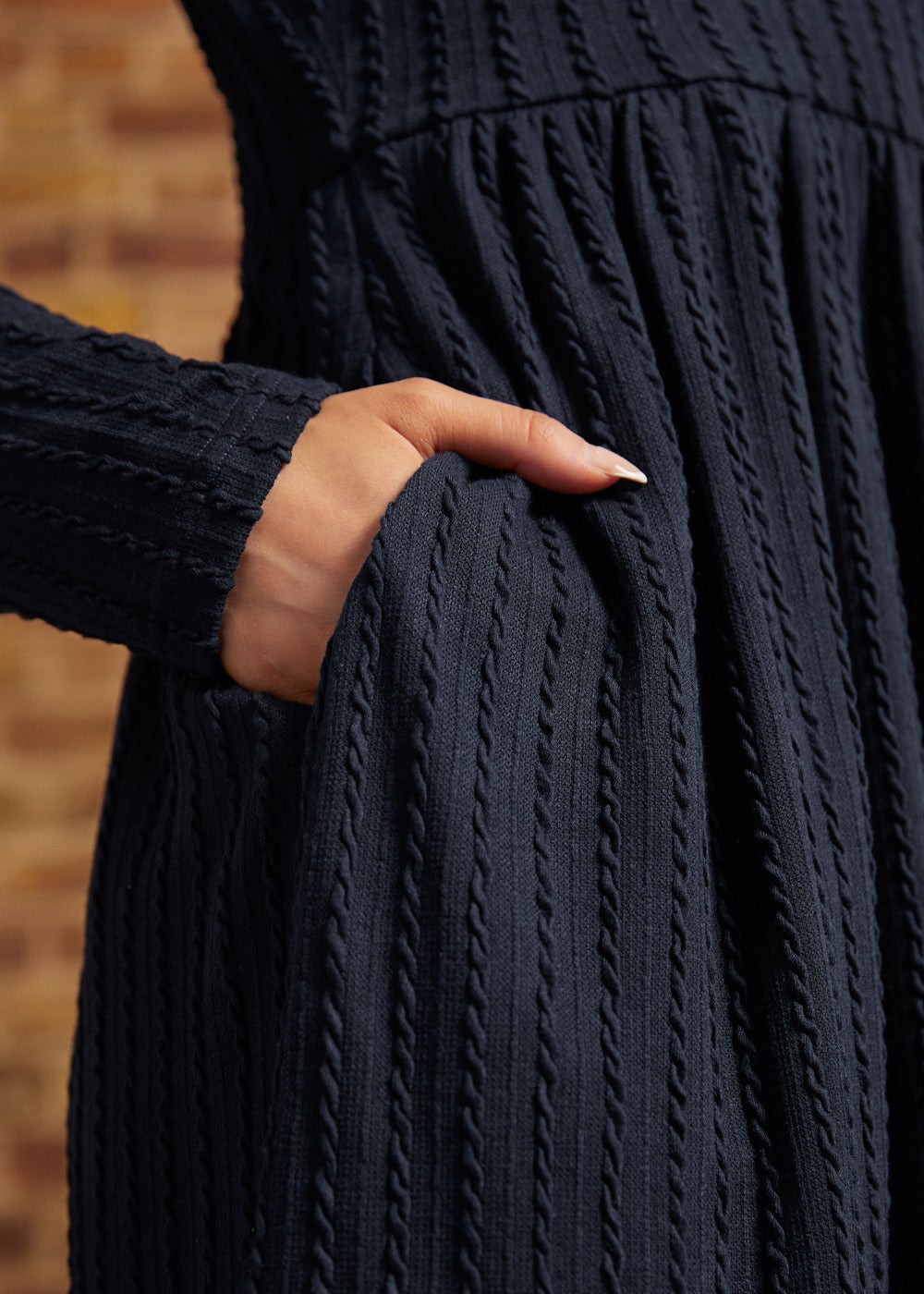 Close-up of hand in side pocket showing the navy textured cable-knit fabric and long sleeves on a ModCloth dress.