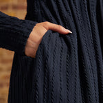 Close-up of hand in side pocket showing the navy textured cable-knit fabric and long sleeves on a ModCloth dress.