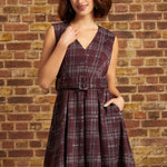 A woman wearing a ModCloth sleeveless V-neck plaid dress with a matching belt, standing against a brick wall background.